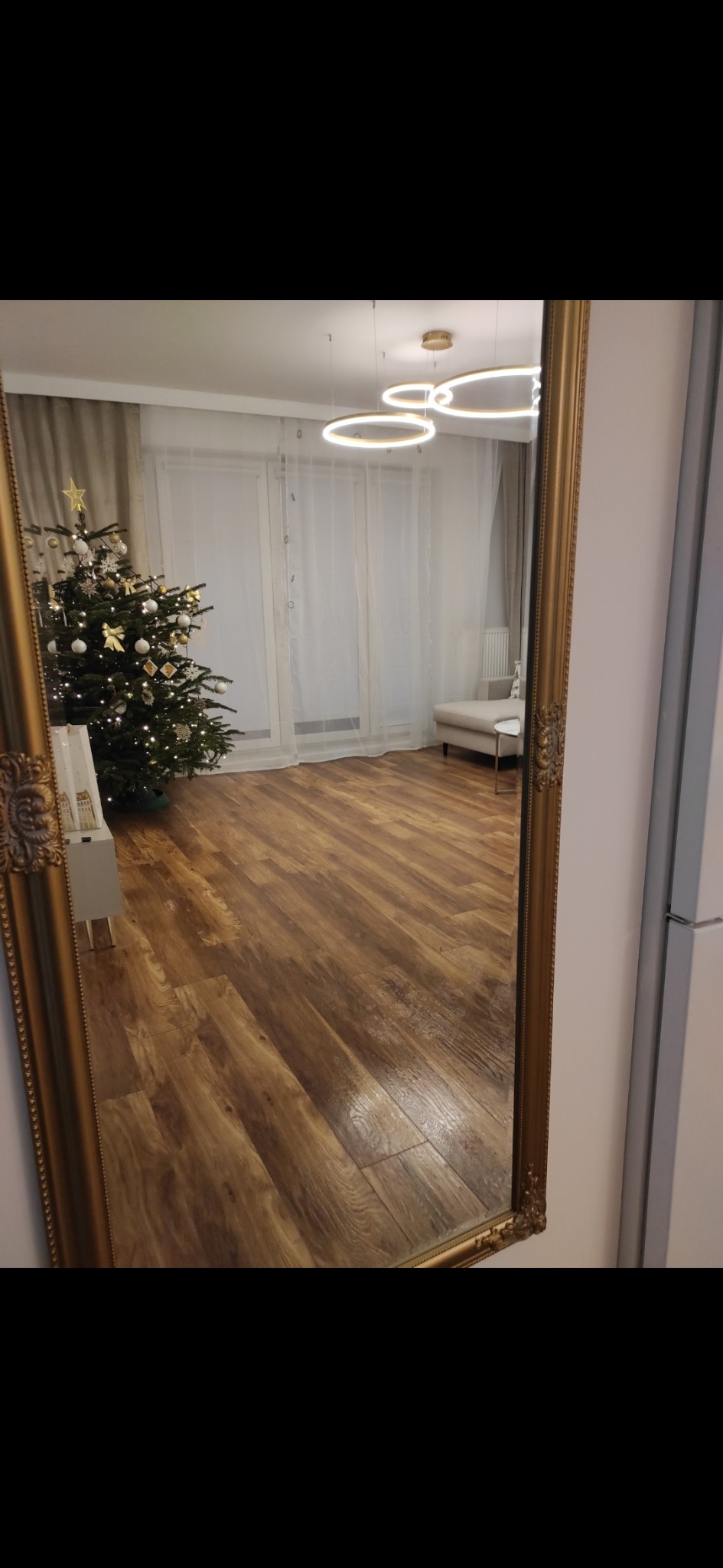 Parkiet ułożony w jodełkę francuską, odbity w ozdobnym lustrze w złotej ramie. W tle choinka, nowoczesne oświetlenie i minimalistyczne meble.