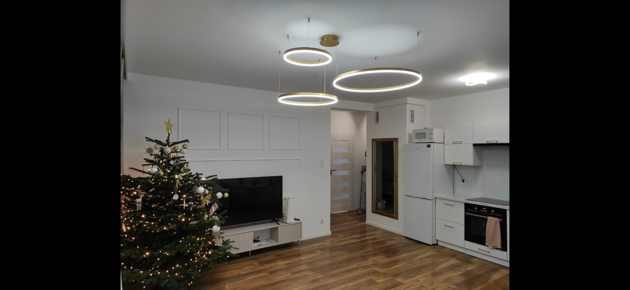 Nowoczesne oświetlenie LED w salonie z aneksem kuchennym w Grodzisku Mazowieckim. Okrągłe lampy wiszące, białe meble i drewniana podłoga tworzą spójną całość.