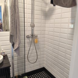 TS Serwis - Nowoczesna kabina prysznicowa z białą, cegiełkową glazurą, czarną mozaiką podłogową i szklaną ścianką. Widoczny ręcznik i armatura.