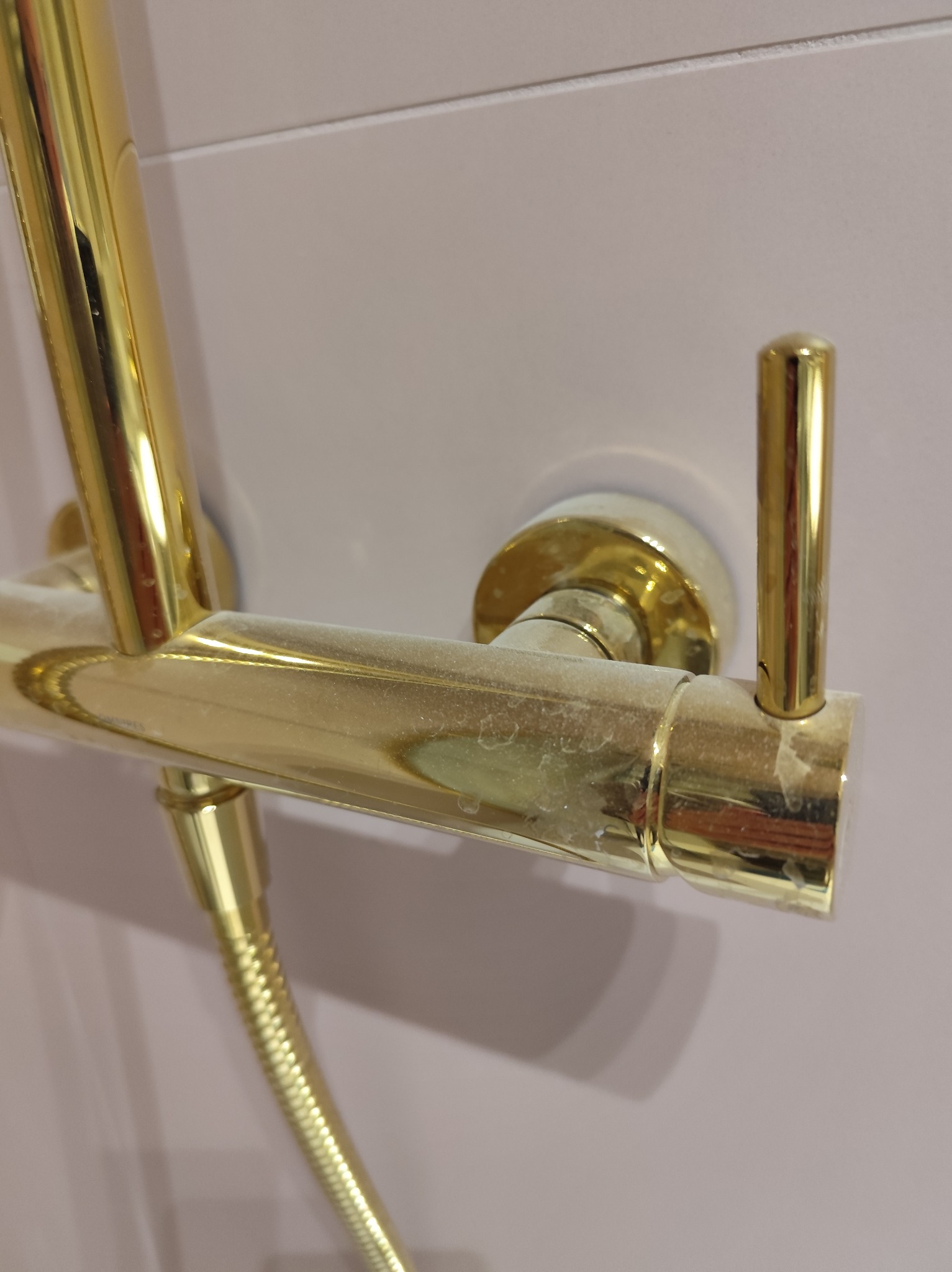 Złota bateria prysznicowa z widocznymi śladami osadu i zacieków, ukazująca potrzebę czyszczenia. Ujęcie z bliska, skupiające się na detalu.