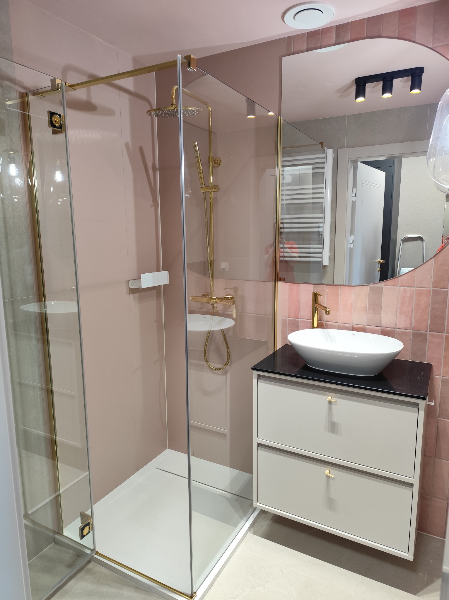 Nowoczesna łazienka z kabiną prysznicową typu walk-in, umywalką nablatową i różowymi płytkami. Złote akcenty armatury i wykończeń dodają elegancji.