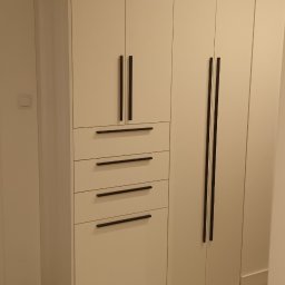Michał Kawka - Biała szafa wnękowa z czterema szufladami i długimi, czarnymi uchwytami, dopasowana do wnętrza. Minimalistyczny design, gładkie fronty, jasna podłoga.