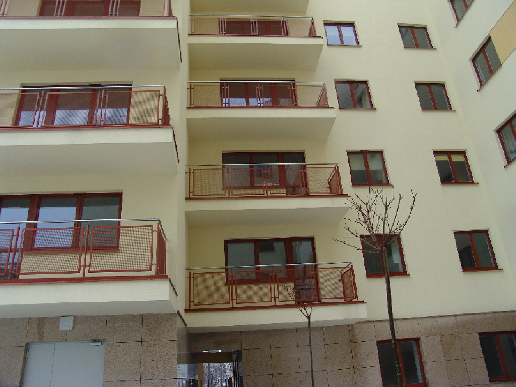 Elewacja budynku wielorodzinnego z balkonami zabezpieczonymi balustradami ze stali nierdzewnej z siatkowym wypełnieniem w kolorze ceglastym, widok z dołu na kilka kondygnacji.