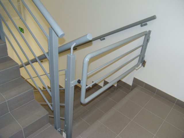 Szare schody z metalową balustradą i dodatkową bramką zabezpieczającą przed wejściem na schody.