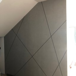 PRIMEKORD - Szara ściana z geometrycznym wzorem czarnych linii w nowoczesnym wnętrzu. Skośny sufit i fragment schodów w tle. Minimalistyczny design.