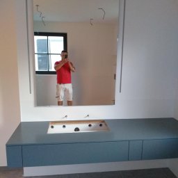 Król Pro - Niebieska szafka pod umywalkę z lustrem w nowoczesnej łazience. Widoczne przygotowane otwory na baterie i odpływ. W lustrze odbija się osoba robiąca zdjęcie.