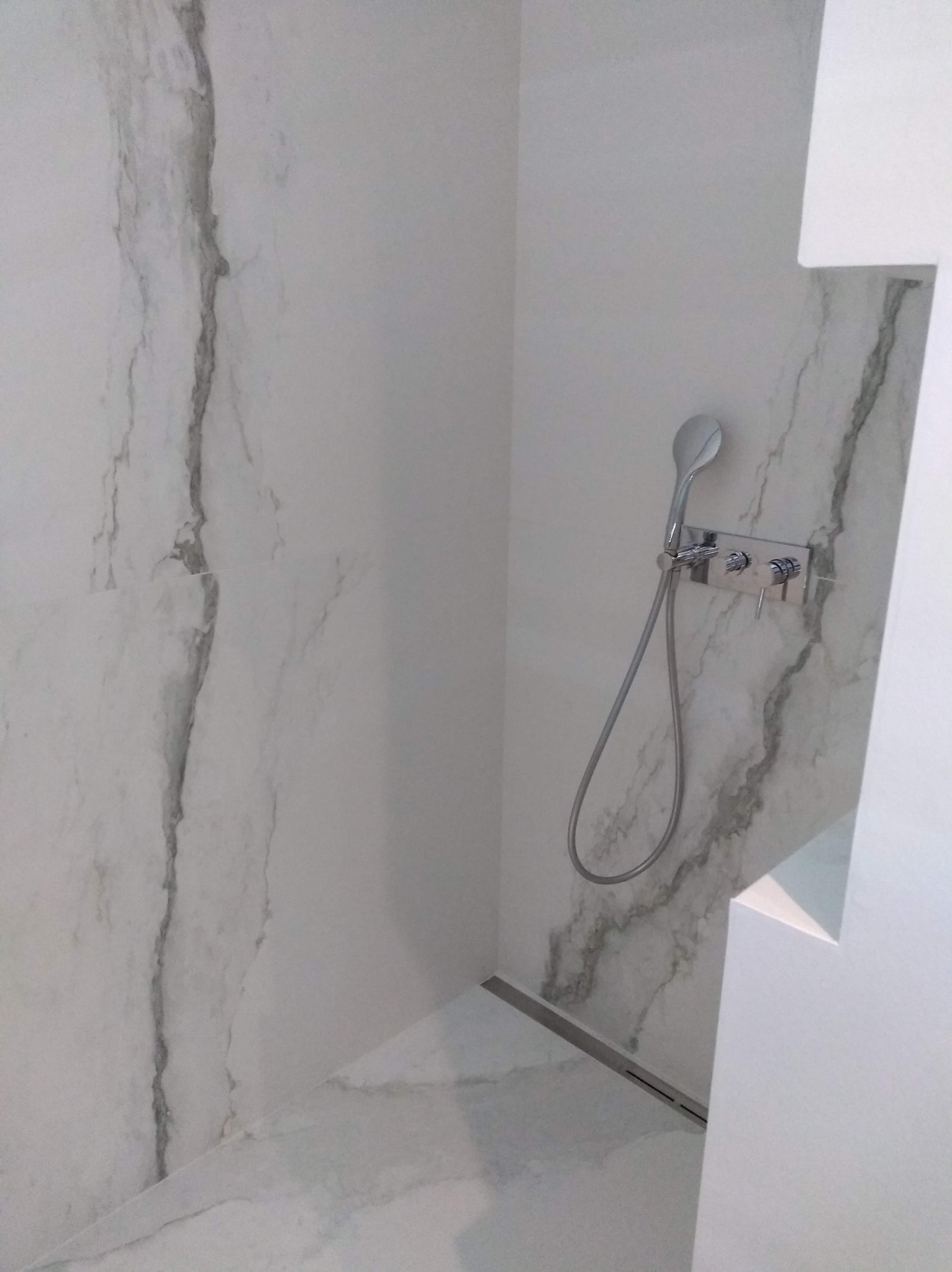 Nowoczesna kabina prysznicowa z marmurowymi płytkami, chromowaną armaturą i odpływem liniowym. Minimalistyczny design, jasne wnętrze, eleganckie wykończenie.