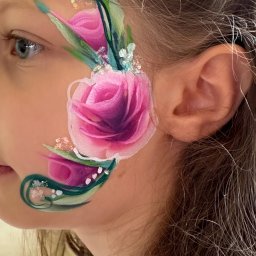 Kreatywne Urodziny Adriana Foryś - Dziewczynka z artystycznym makijażem twarzy, przedstawiającym różę z zielonymi pędami i białymi akcentami. Widoczny profil twarzy i fragment włosów.