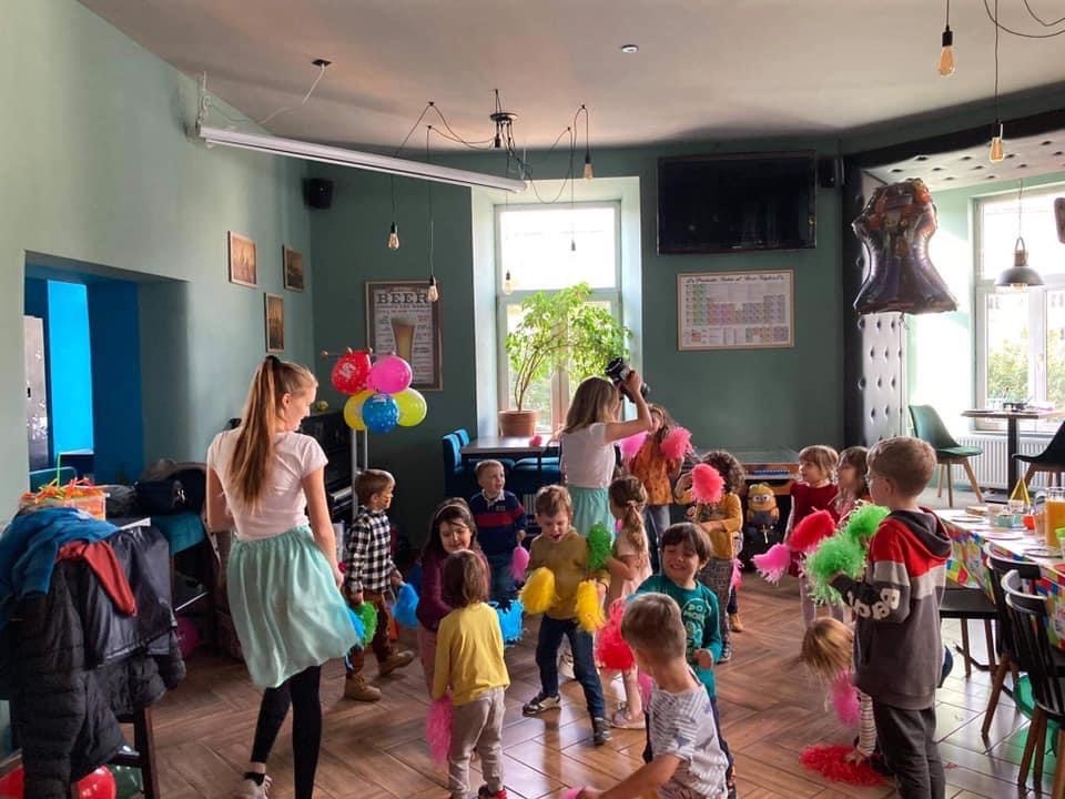 Animator w akcji podczas urodzin dziecka w Krakowie. Dzieci z kolorowymi pomponami, balony, dekoracje. Radosna atmosfera zabawy.