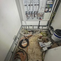 Filip Dytman - Rozdzielnia elektryczna w trakcie montażu, widoczne kable, skrzynka z bezpiecznikami i narzędzia. Ujęcie z góry, ukazujące etap prac instalacyjnych.