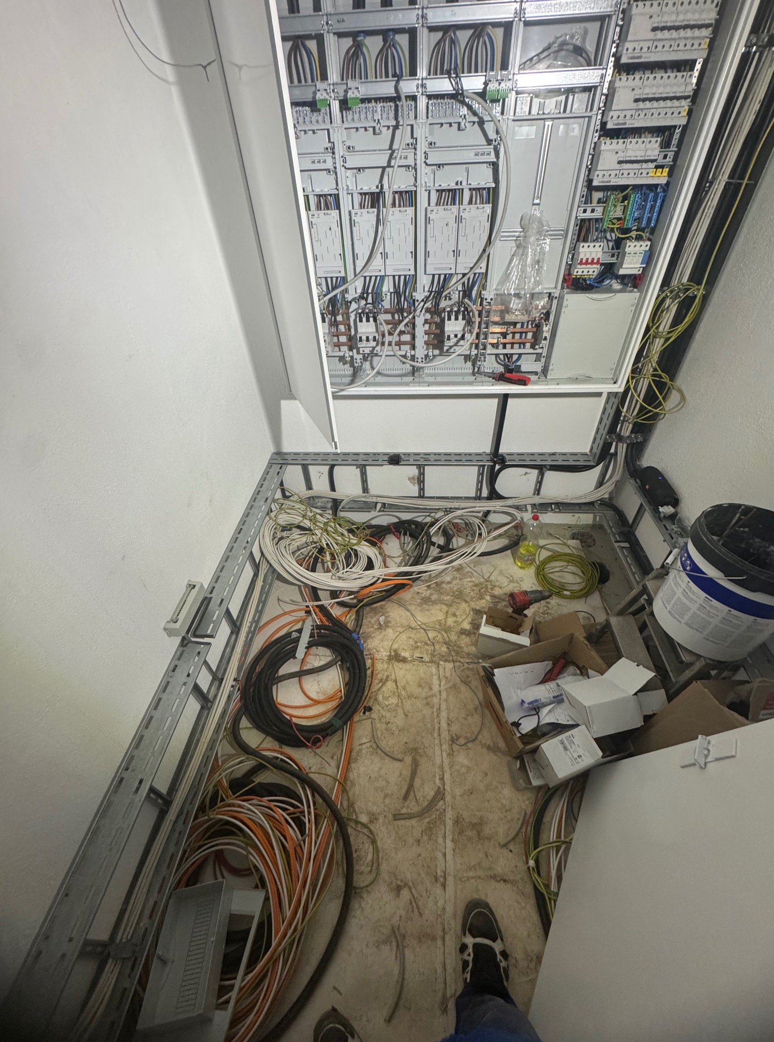 Rozdzielnia elektryczna w trakcie montażu, widoczne kable, skrzynka z bezpiecznikami i narzędzia. Ujęcie z góry, ukazujące etap prac instalacyjnych.