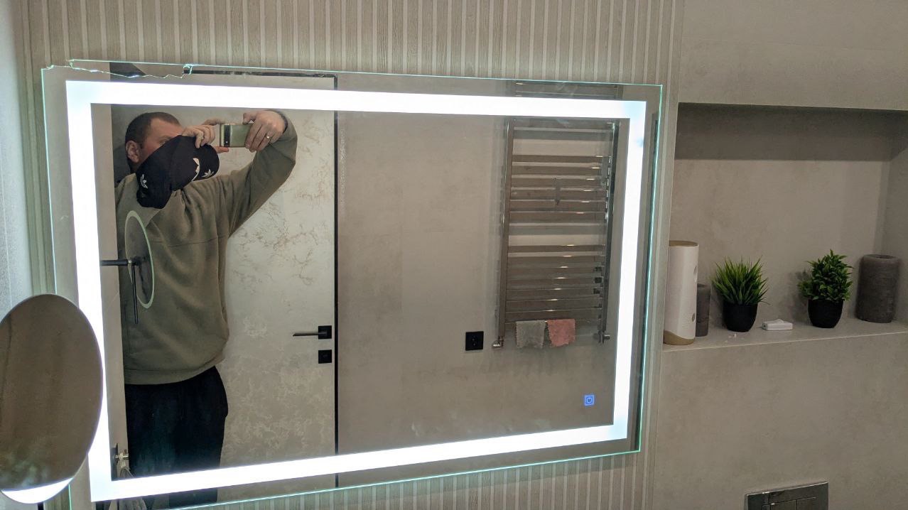 Nowoczesne lustro z podświetleniem LED w łazience po remoncie w Katowicach. Widoczne odbicie osoby robiącej zdjęcie. Minimalistyczny design i funkcjonalne oświetlenie.