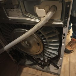 ELEKTRO AL SPÓŁKA Z OGRANICZONĄ ODPOWIEDZIALNOŚCIĄ - Otwarta obudowa pralki z widocznym bębnem i wężem odpływowym. Widoczne elementy mechaniczne i elektryczne. Ujęcie z bliska, ukazujące wnętrze urządzenia.