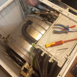 ELEKTRO AL SPÓŁKA Z OGRANICZONĄ ODPOWIEDZIALNOŚCIĄ - Wnętrze pralki w trakcie naprawy: bęben, przewody, narzędzia (kombinerki i śrubokręt). Widoczne elementy konstrukcyjne i podzespoły urządzenia. Ujęcie z góry, w trakcie serwisu.