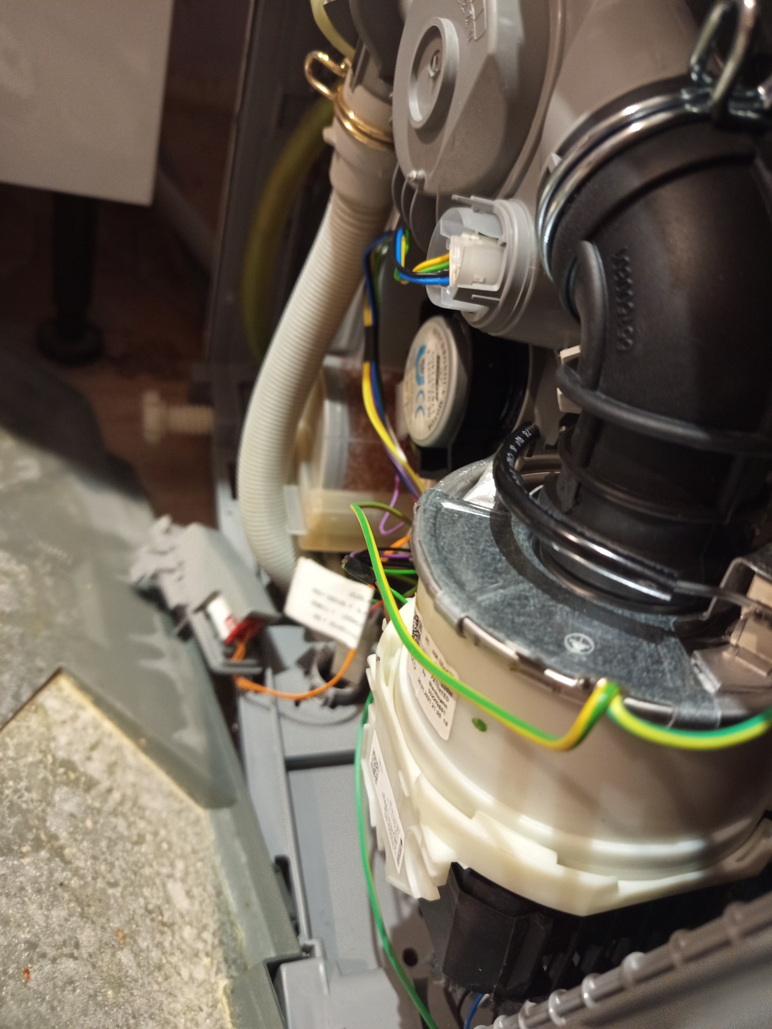 Wnętrze zmywarki w trakcie naprawy: widoczne przewody, węże i elementy pompy obiegowej. Skupienie na detalach techniczych, oświetlenie punktowe.