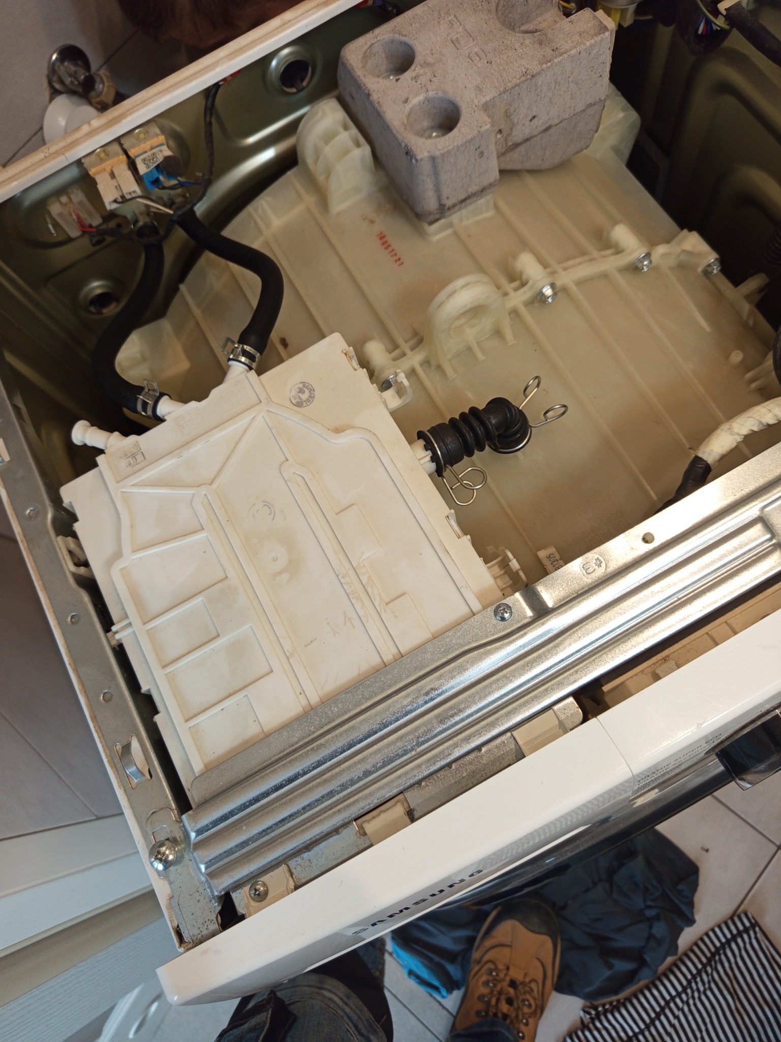 Wnętrze pralki Samsung z widocznymi elementami konstrukcyjnymi i podzespołami podczas naprawy. Widoczne przewody, zbiornik i obciążnik betonowy.