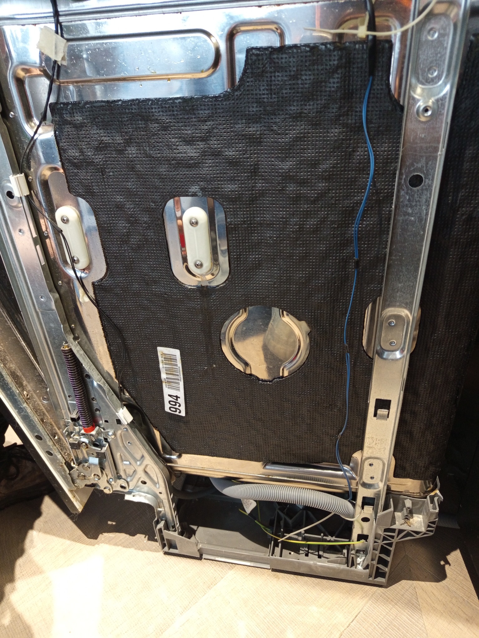 Wnętrze zmywarki z widoczną izolacją, elementami metalowymi i przewodami. Detal z bliska, ukazujący konstrukcję i komponenty urządzenia AGD.