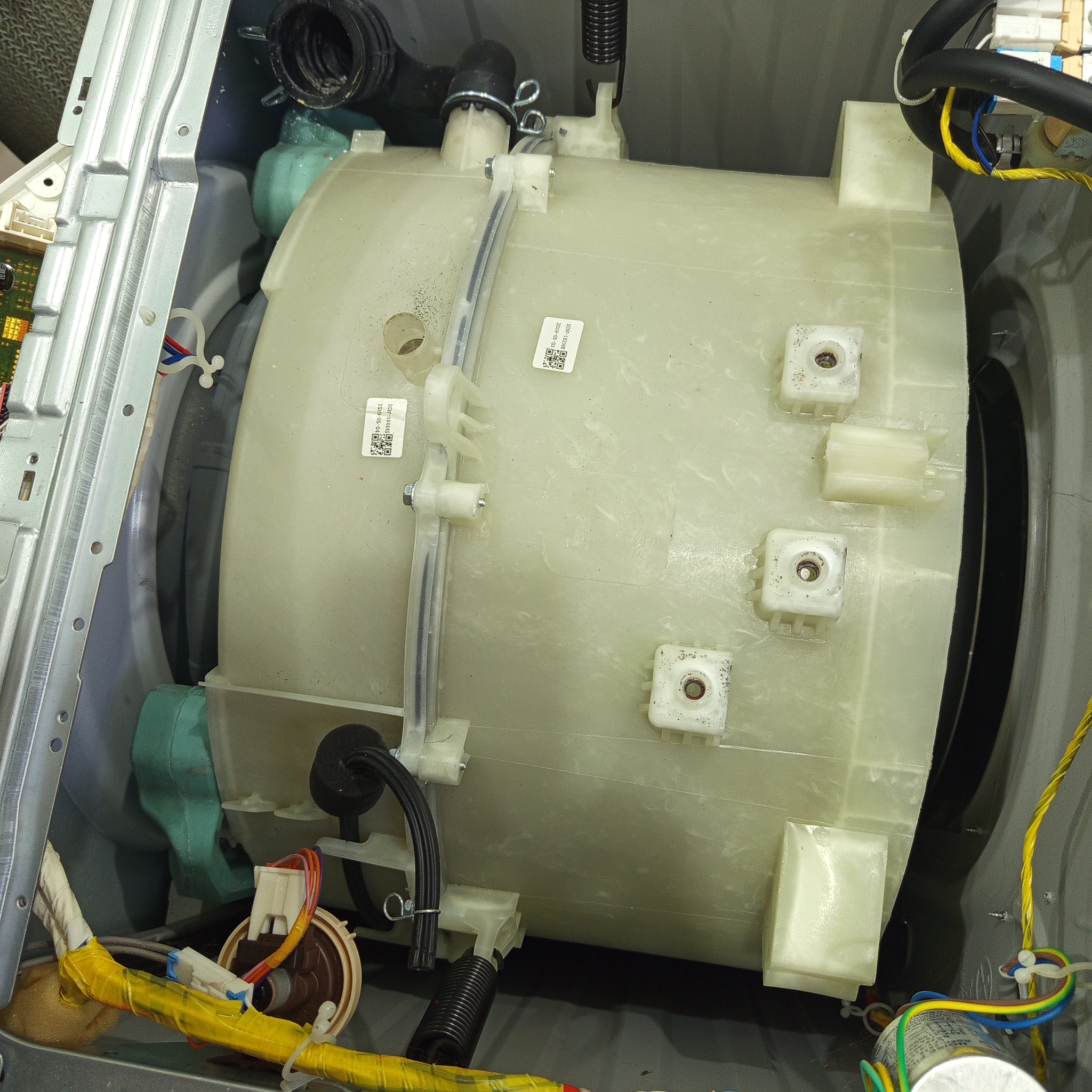 Wnętrze pralki automatycznej z widocznym bębnem, elementami mocującymi i przewodami. Ukazane detale konstrukcyjne urządzenia AGD w trakcie naprawy.