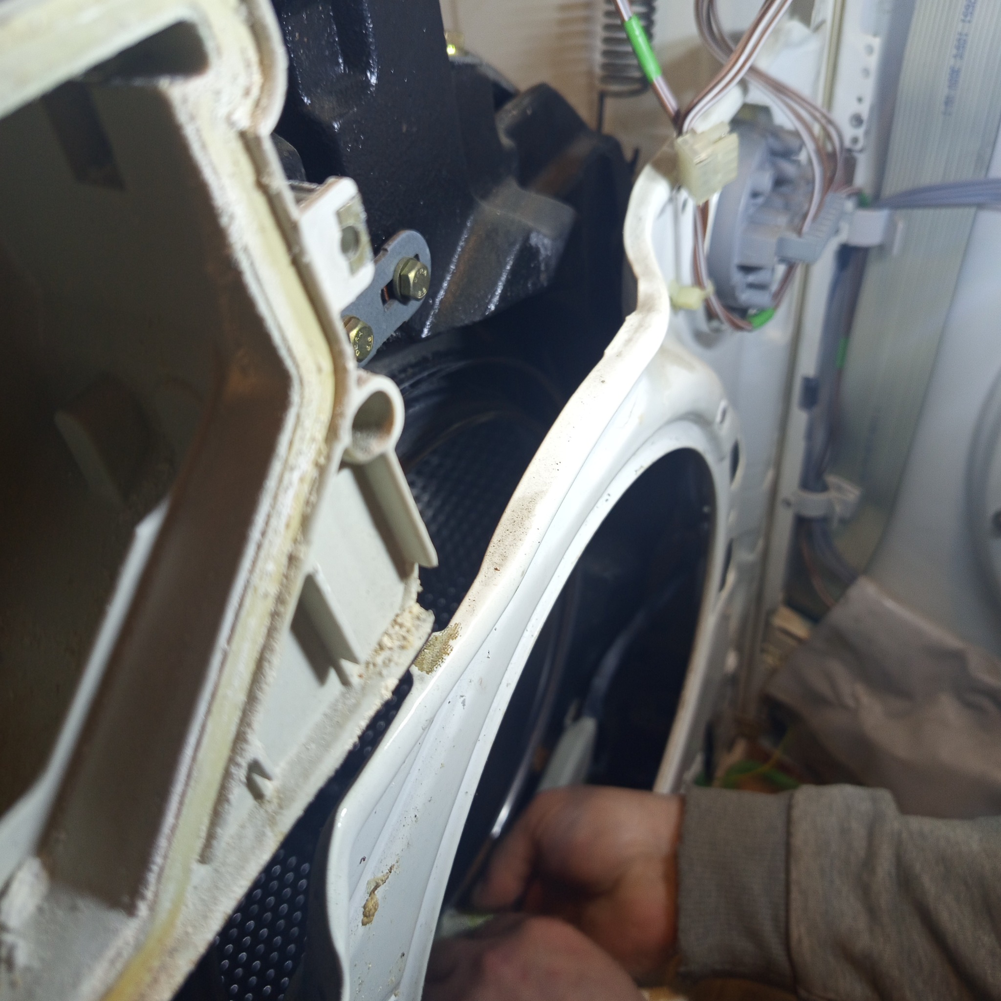 Wnętrze pralki w trakcie naprawy: widoczne elementy konstrukcyjne, bęben i ręce serwisanta przy pracy. Detal z bliska, oświetlenie robocze.