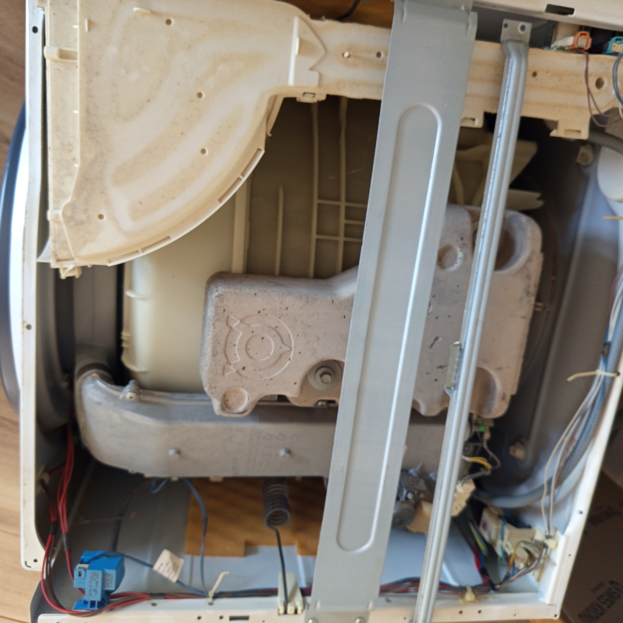 Wnętrze pralki automatycznej z widocznymi elementami konstrukcyjnymi i przewodami elektrycznymi. Detaliczny widok na podzespoły podczas naprawy.