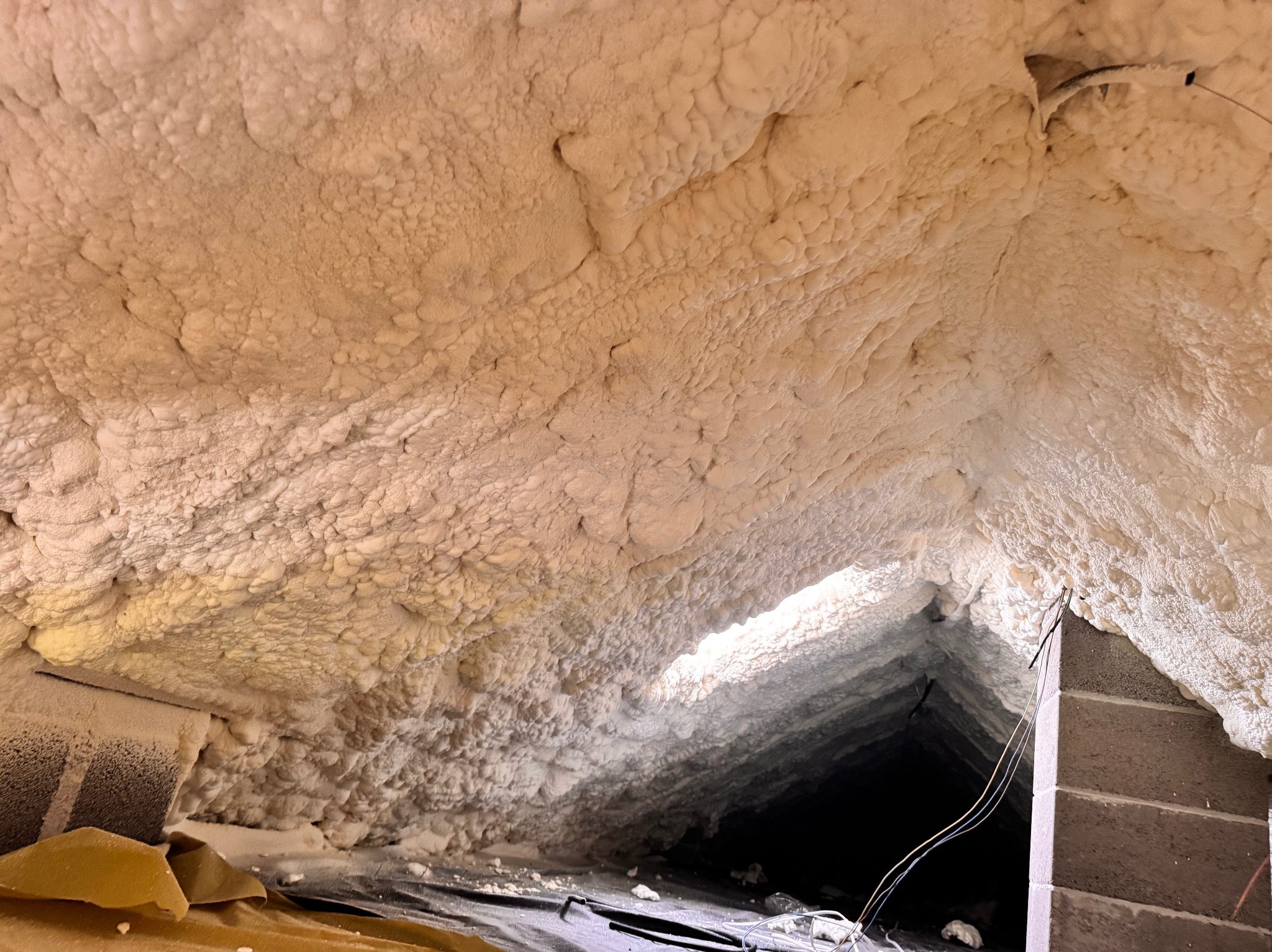 Ocieplenie poddasza pianką PUR, widok z dołu. Aplikacja pianki na skośnych powierzchniach, widoczne detale struktury pianki i elementy konstrukcyjne poddasza.