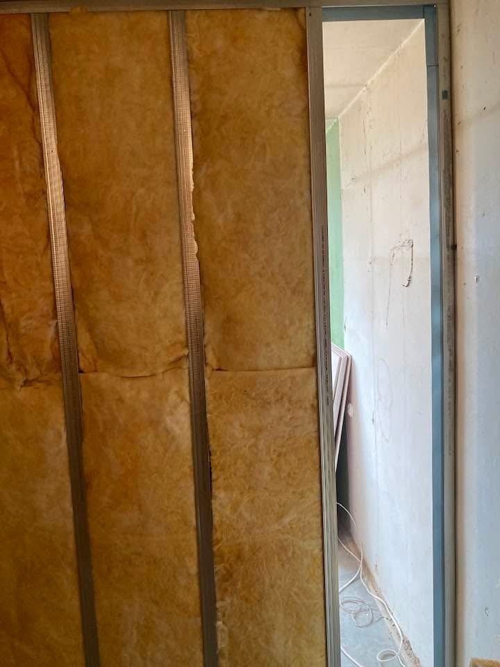 Ocieplenie ściany wełną mineralną w metalowym stelażu. Widoczne niedoskonałości w ułożeniu izolacji i surowy stan wykończenia wnętrza.