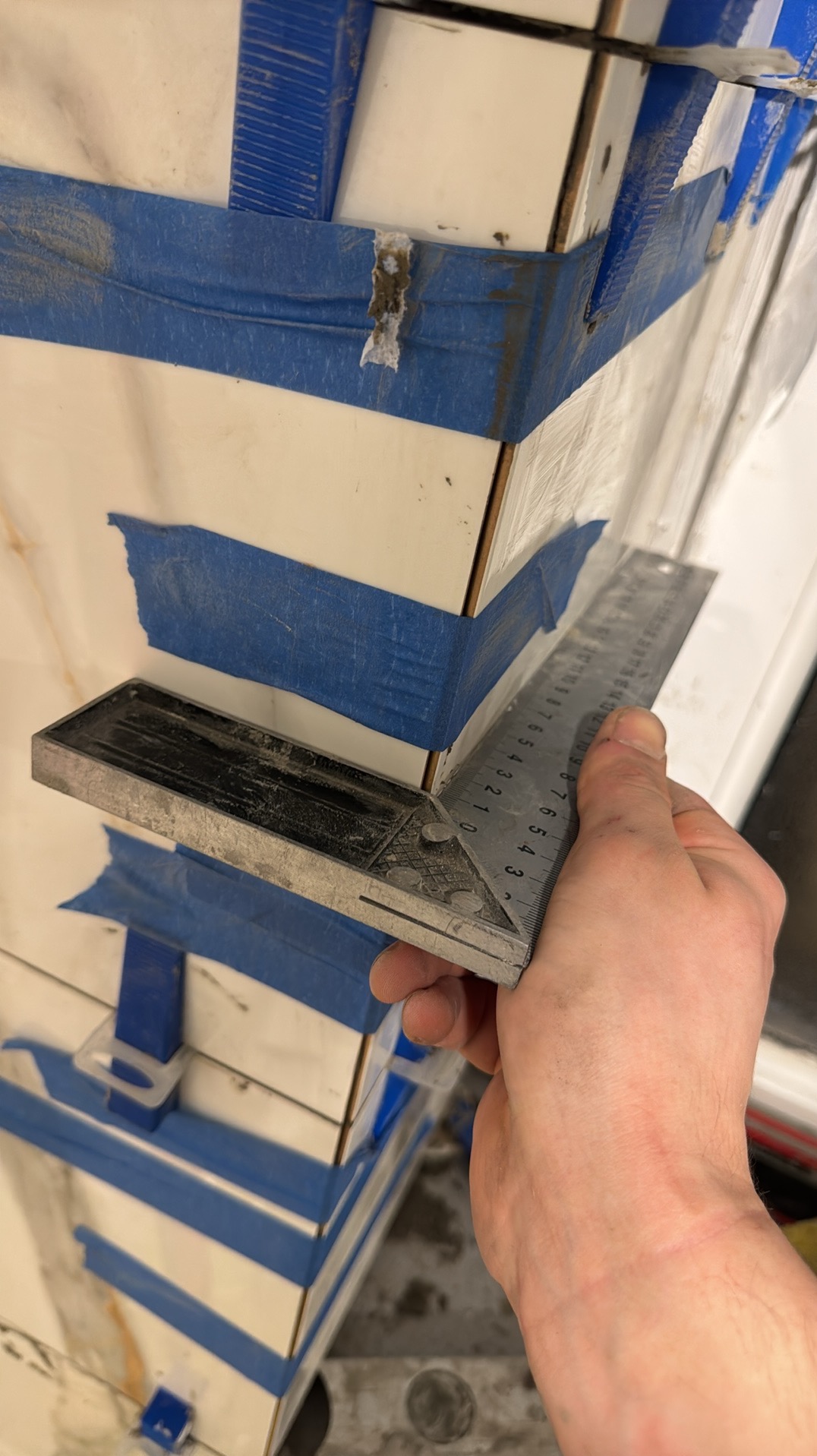 Układanie płytek narożnych z użyciem kątownika i taśmy maskującej. Detal wykończenia, precyzja montażu, widoczne narzędzie pracy glazurnika.