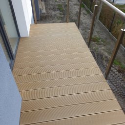 Usługi remontowe Łukasz Majewski - Nowoczesny balkon z desek kompozytowych w odcieniach beżu, wykończony metalową balustradą. Widok z góry na ułożone deski i fragment elewacji budynku.