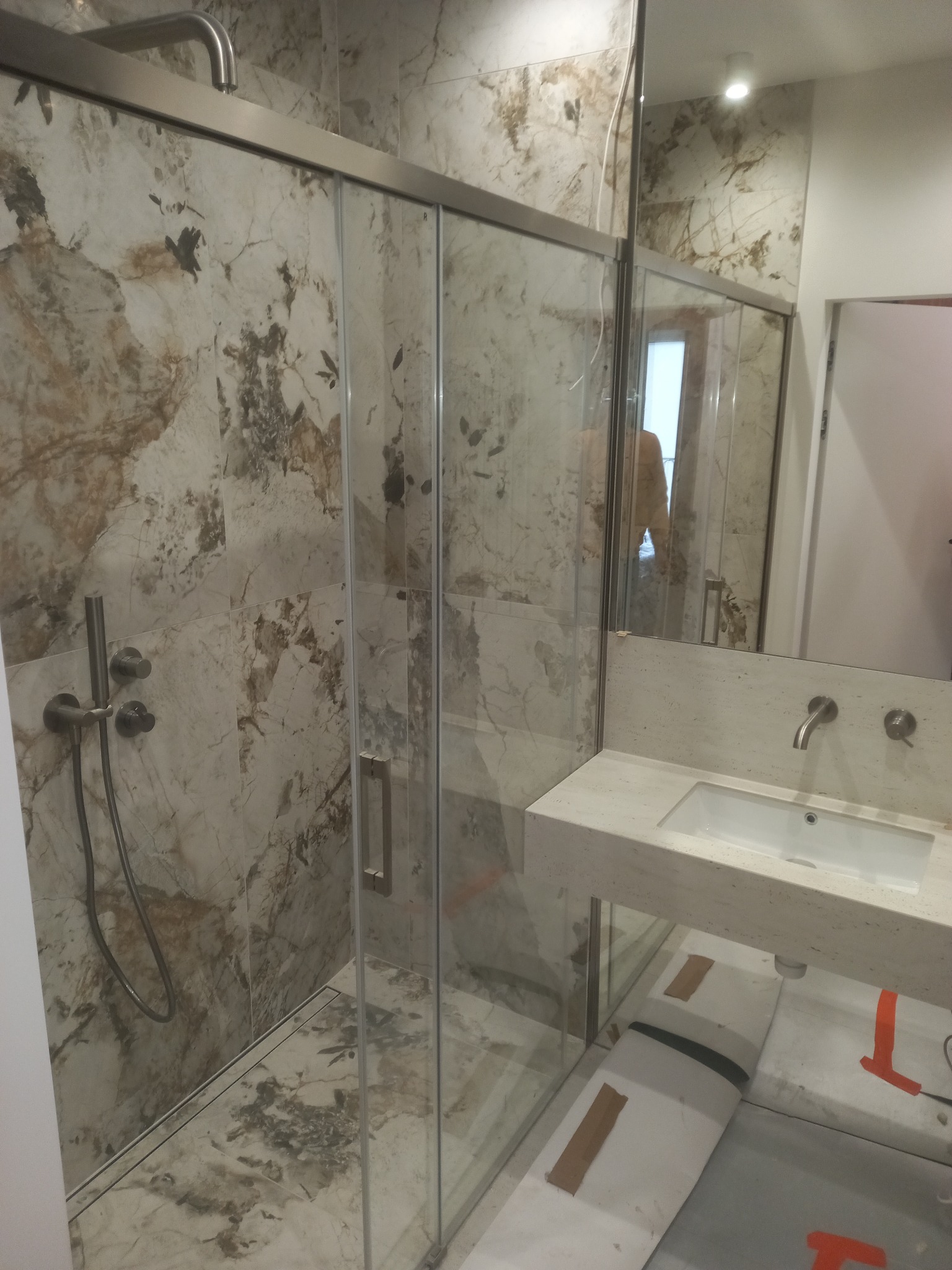 Wykończona łazienka z kabiną prysznicową typu walk-in, marmurowe płytki na ścianach i podłodze, minimalistyczna umywalka nablatowa. Nowoczesny design.