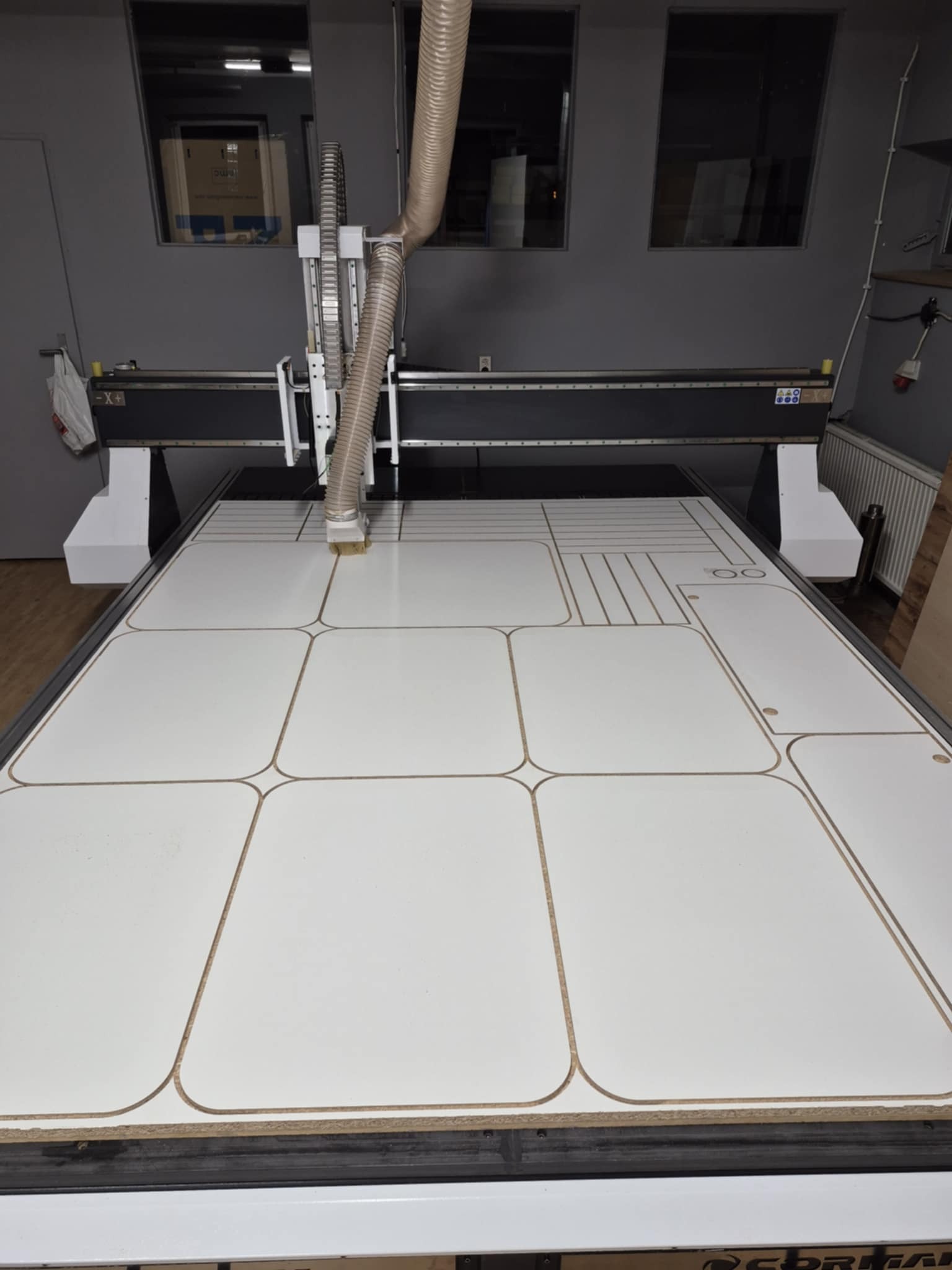 Obróbka CNC w Katowicach: Frezarka CNC w trakcie pracy nad płytą meblową z wyfrezowanymi wzorami. Widoczne detale obróbki i precyzja wykonania.