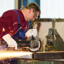 Etat-Hr - Pracownik w okularach ochronnych szlifuje metalową konstrukcję szlifierką kątową, iskry rozbryzgują się na boki. Praca z metalem, bezpieczeństwo, odzież robocza.