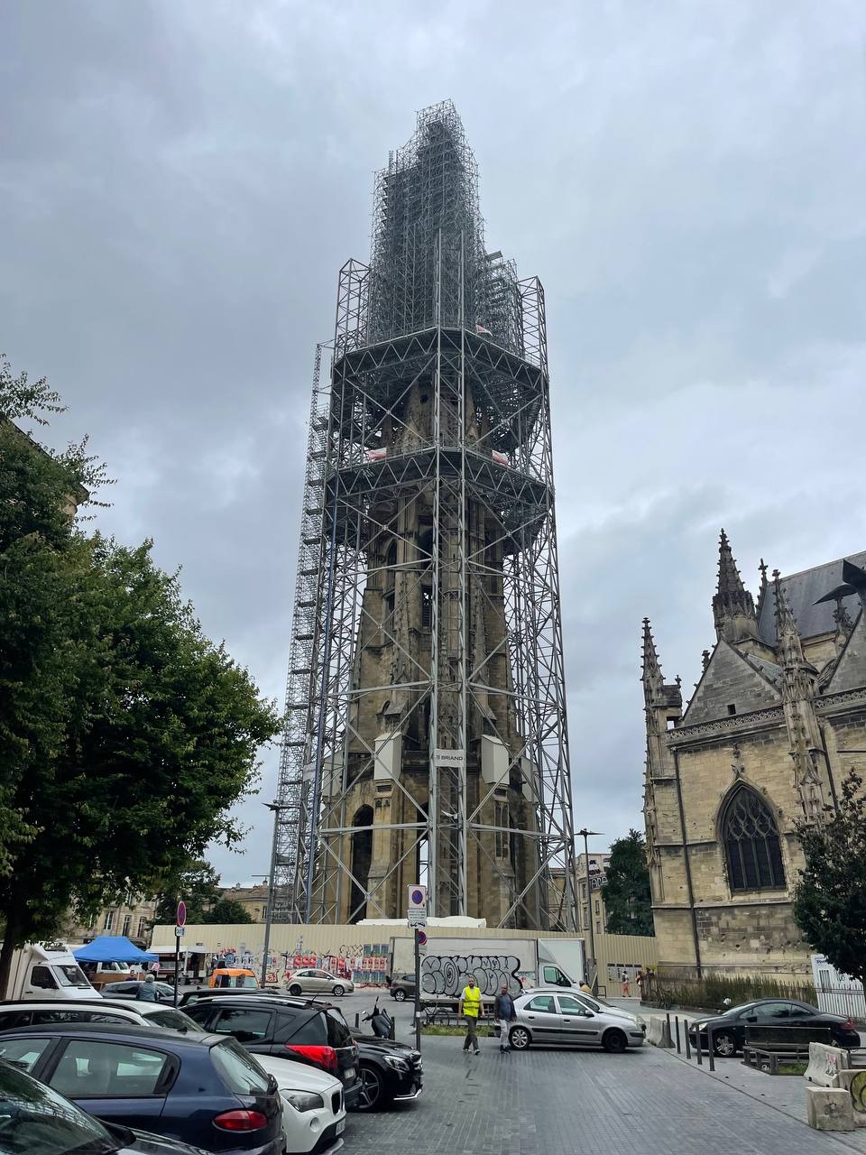 Wysoka wieża kościoła otoczona rusztowaniami, przygotowywana do prac renowacyjnych. Widoczne fragmenty elewacji i detale architektoniczne. Pochmurne niebo w tle.