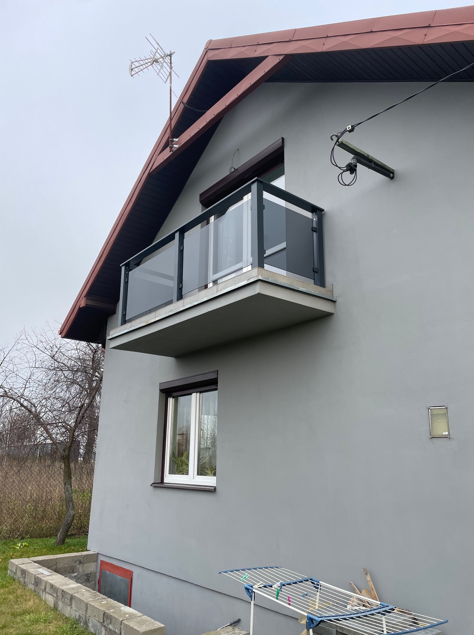 Szklana balustrada na balkonie domu o szarej elewacji. Widoczne detale mocowania i konstrukcja. Ujęcie z dołu, podkreślające nowoczesny design.