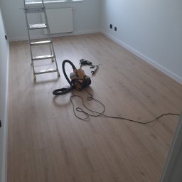 Oleksandr Partala - Jasne panele podłogowe w pokoju po remoncie, drabina malarska, odkurzacz i narzędzia na podłodze. Świeżo pomalowane ściany i listwy przypodłogowe.