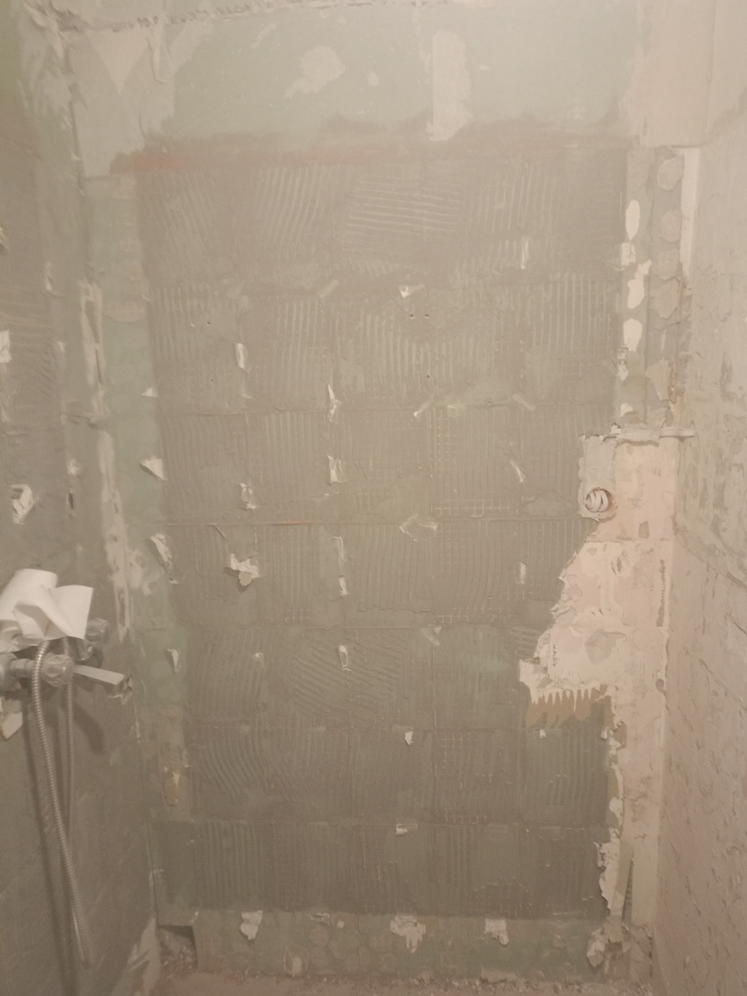 Ściana w trakcie przygotowania do położenia płytek w łazience. Widoczne ślady po usuniętych płytkach i nałożony klej. Fragment instalacji wodnej.