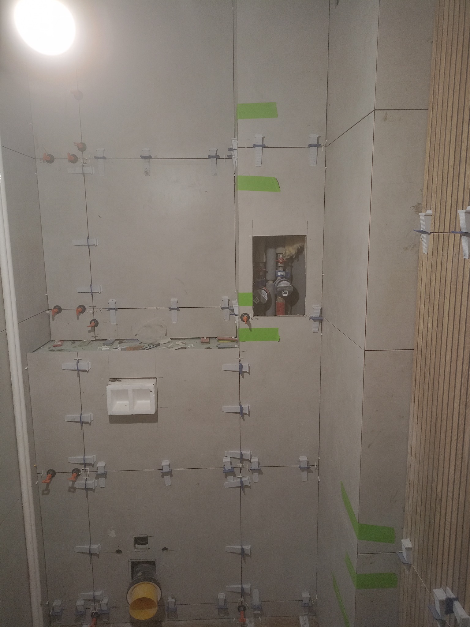 Łazienka w trakcie remontu: ułożone płytki ceramiczne na ścianach, z użyciem krzyżyków dystansowych i poziomicy laserowej. Widoczne pionowe panele dekoracyjne.