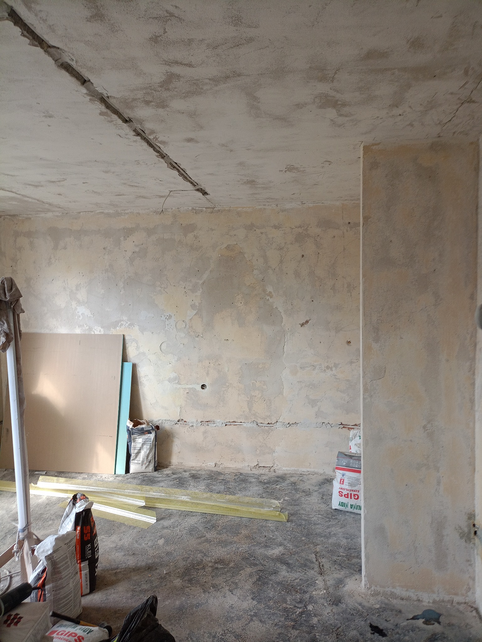 Przygotowanie do gładzi w Toruniu: surowe ściany, płyty gipsowe, worki z gipsem i profile narożnikowe. Widoczne ślady po instalacjach elektrycznych.