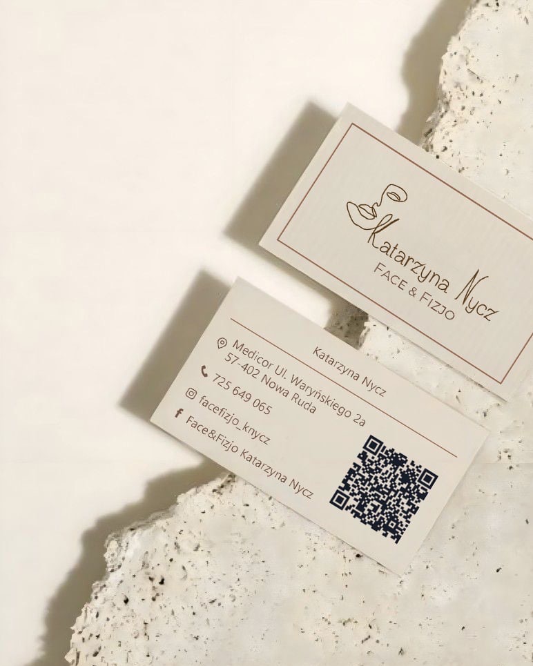 Dwie wizytówki z danymi firmy 'Katarzyna Nycz FACE & FIZJO' na teksturowanym, jasnym tle. Jedna z kodem QR, druga z minimalistycznym logo przedstawiającym kontur twarzy.