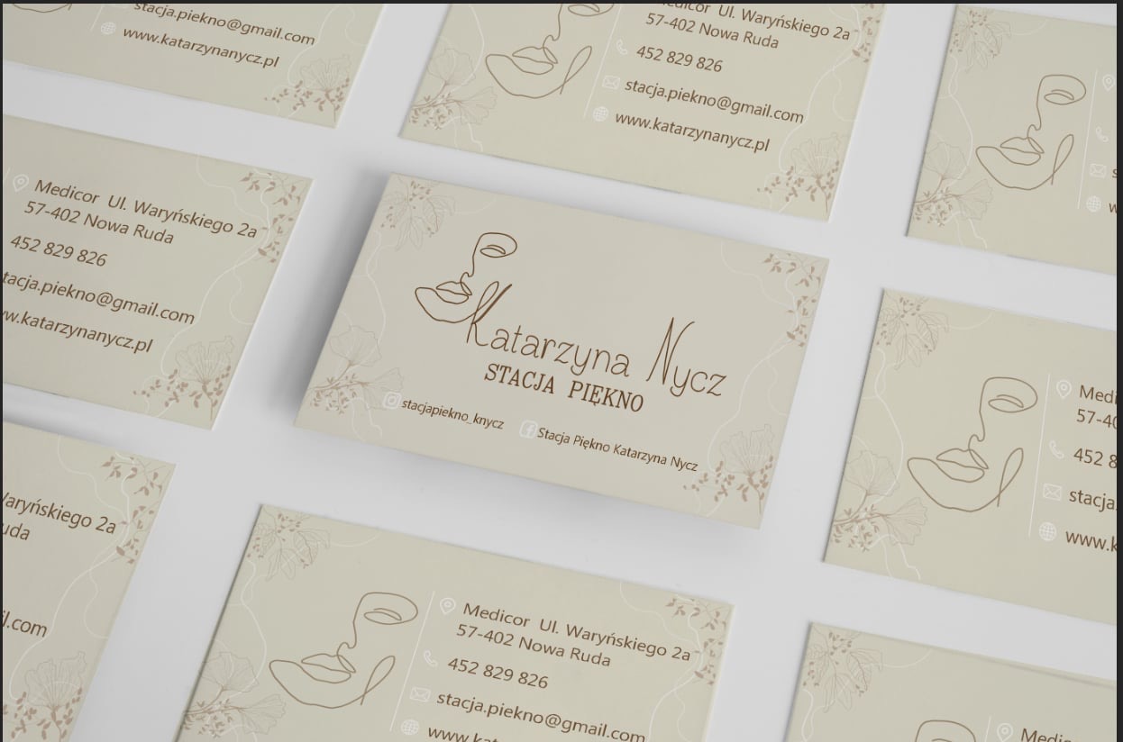Eleganckie wizytówki w odcieniach beżu z minimalistycznym rysunkiem twarzy i motywami roślinnymi, ułożone pod kątem na jasnym tle. Subtelny design dla salonu kosmetycznego.