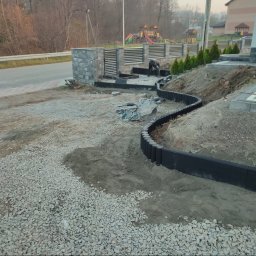 Podhale Invest Bud - Krawężnik z palisady w ogrodzie, wyznaczający ścieżkę. W tle widoczny pracownik, narzędzia i plac zabaw. Palisada w kolorze czarnym, ułożona w łagodny łuk.