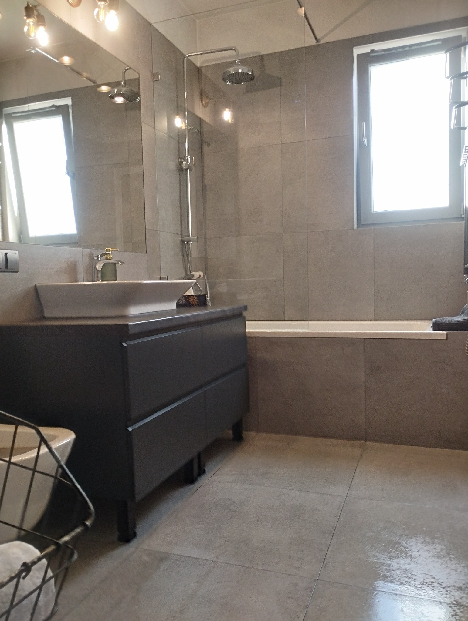 Nowoczesna łazienka w szarościach: umywalka nablatowa na szafce, kabina prysznicowa typu walk-in, okno z widokiem na zewnątrz. Minimalistyczny design, czyste linie.