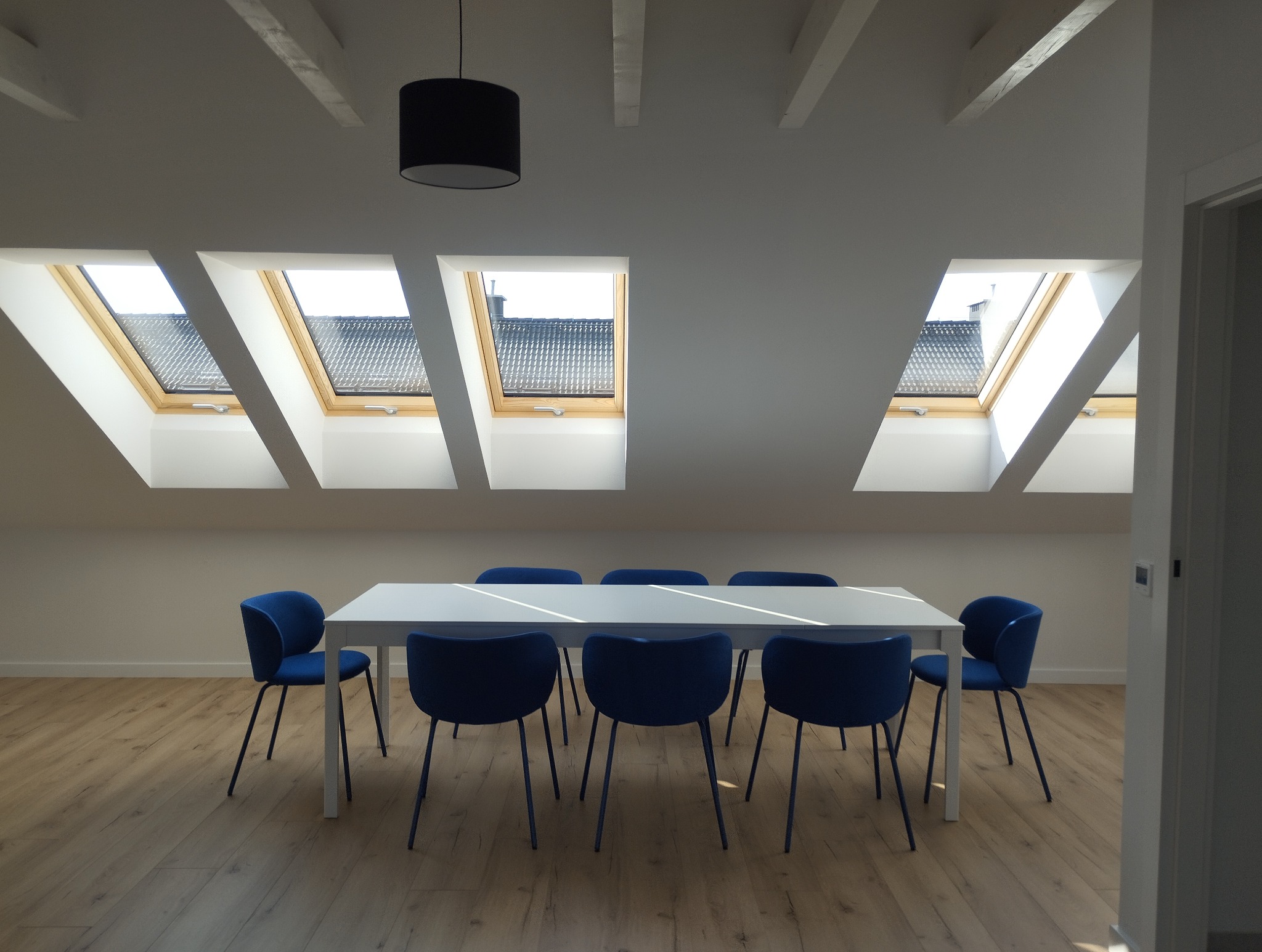 Jasne poddasze we Wrocławiu po remoncie: białe ściany, drewniana podłoga, okna dachowe i niebieskie krzesła wokół białego stołu. Minimalistyczny design.