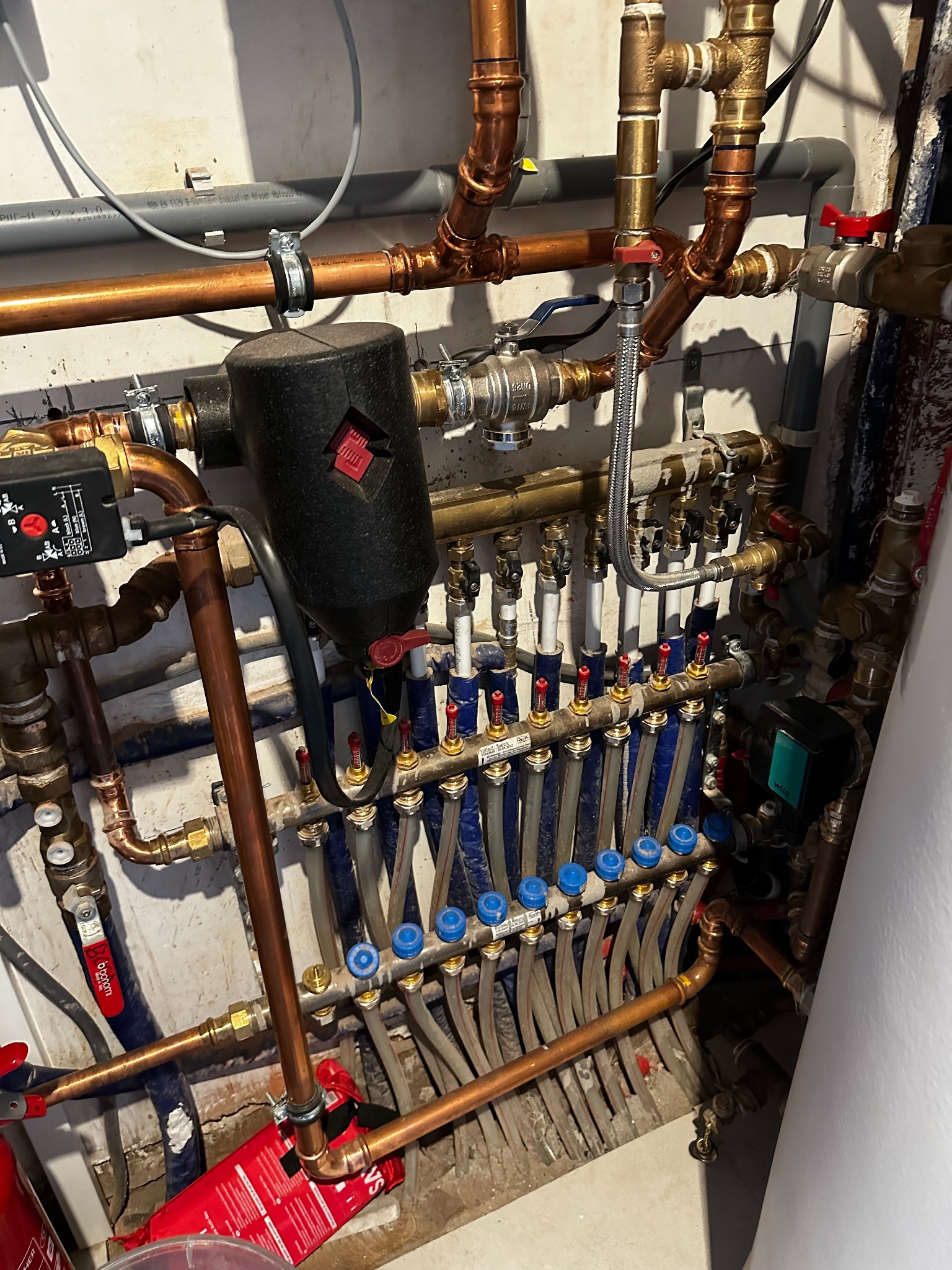 Rozbudowana instalacja hydrauliczna z miedzianymi rurami, zaworami i rozdzielaczem, widoczna w kotłowni. Elementy połączone, gotowe do użytku.