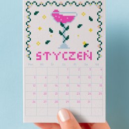 Kreatywka - Kalendarz na styczeń z grafiką koktajlu w stylu haftu krzyżykowego, trzymany w dłoni na tle błękitnej ściany. Unikalny, ręcznie robiony design.