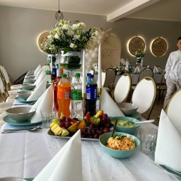 ADbiuro Dorota Adamowska - Uroczysty stół komunijny z białym obrusem zdobionym perłami, kwiatami, napojami i sałatkami. W tle dekoracje z balonów i podświetlane napisy.