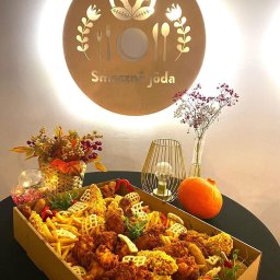 ADbiuro Dorota Adamowska - Dekoracyjna skrzynia z frytkami, kurczakiem i goframi, podświetlona logo 'Smaczna Jôda', obok dynia i kwiaty. Elegancka prezentacja dań.