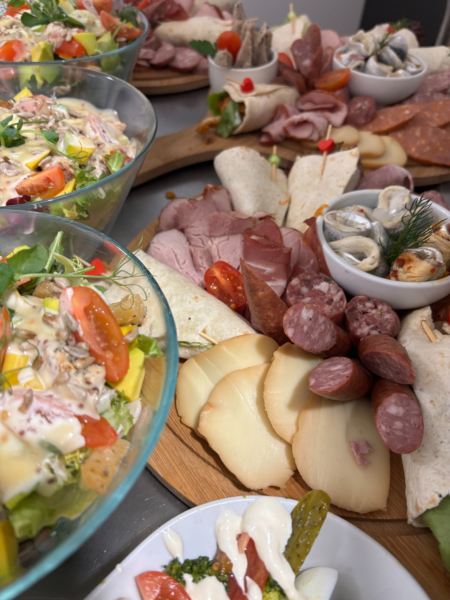 Bogato zastawiony stół z deskami serów, wędlin, sałatkami w szklanych misach i tortillami. Różnorodność przekąsek na przyjęcie, widok z góry, ciepłe oświetlenie.