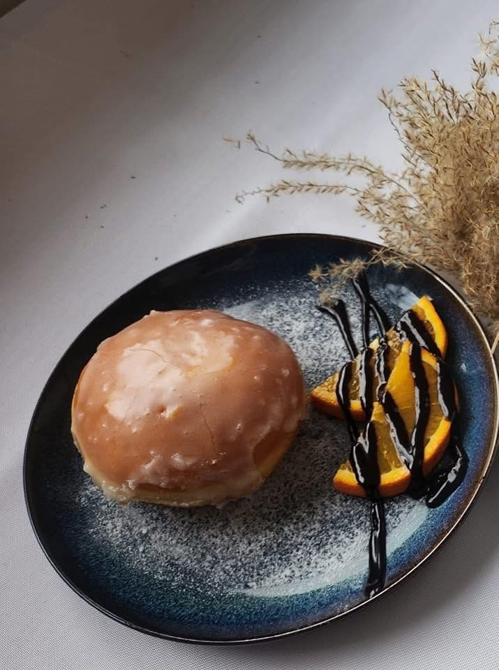 Pączek z lukrem i pomarańczami polanymi czekoladą na talerzu w stylu vintage, posypanym cukrem pudrem. Dekoracja z suszonych traw w tle.