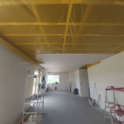 DDD FORTE Tomasz Wesołowski - Montaż sufitu podwieszanego z płyt gipsowo-kartonowych w nowym wnętrzu. Widoczne rusztowanie, profile i folia ochronna. Prace w toku, sufit częściowo zamontowany.