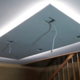 DDD FORTE Tomasz Wesołowski - Podwieszany sufit z płyty z oświetleniem LED, widoczne kable, fragment schodów w tle. Kształt sufitu prostokątny z zaokrąglonymi rogami.